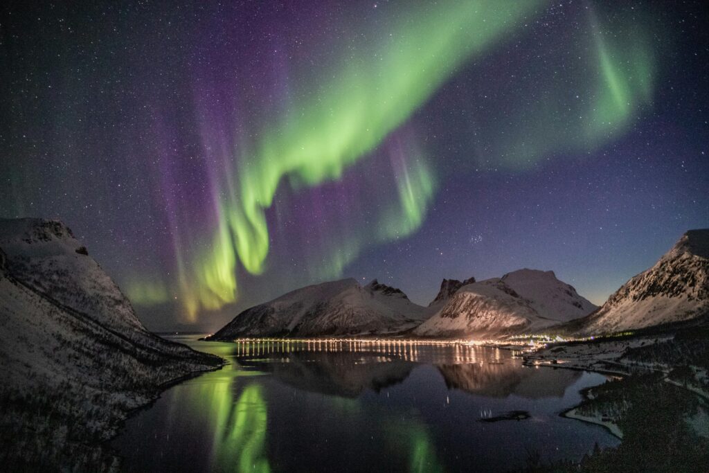 Norway -- northern lights over town at bottom of fjords